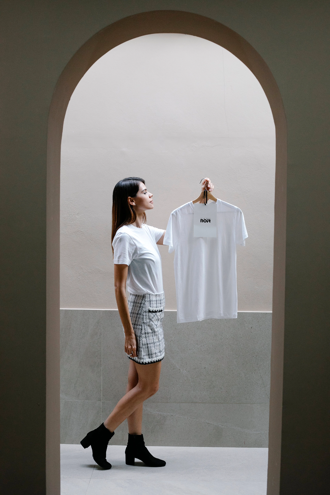 Женщина держит футболку с лейблом Atelier NOIR в ярком интерьере, брендирование одежды.