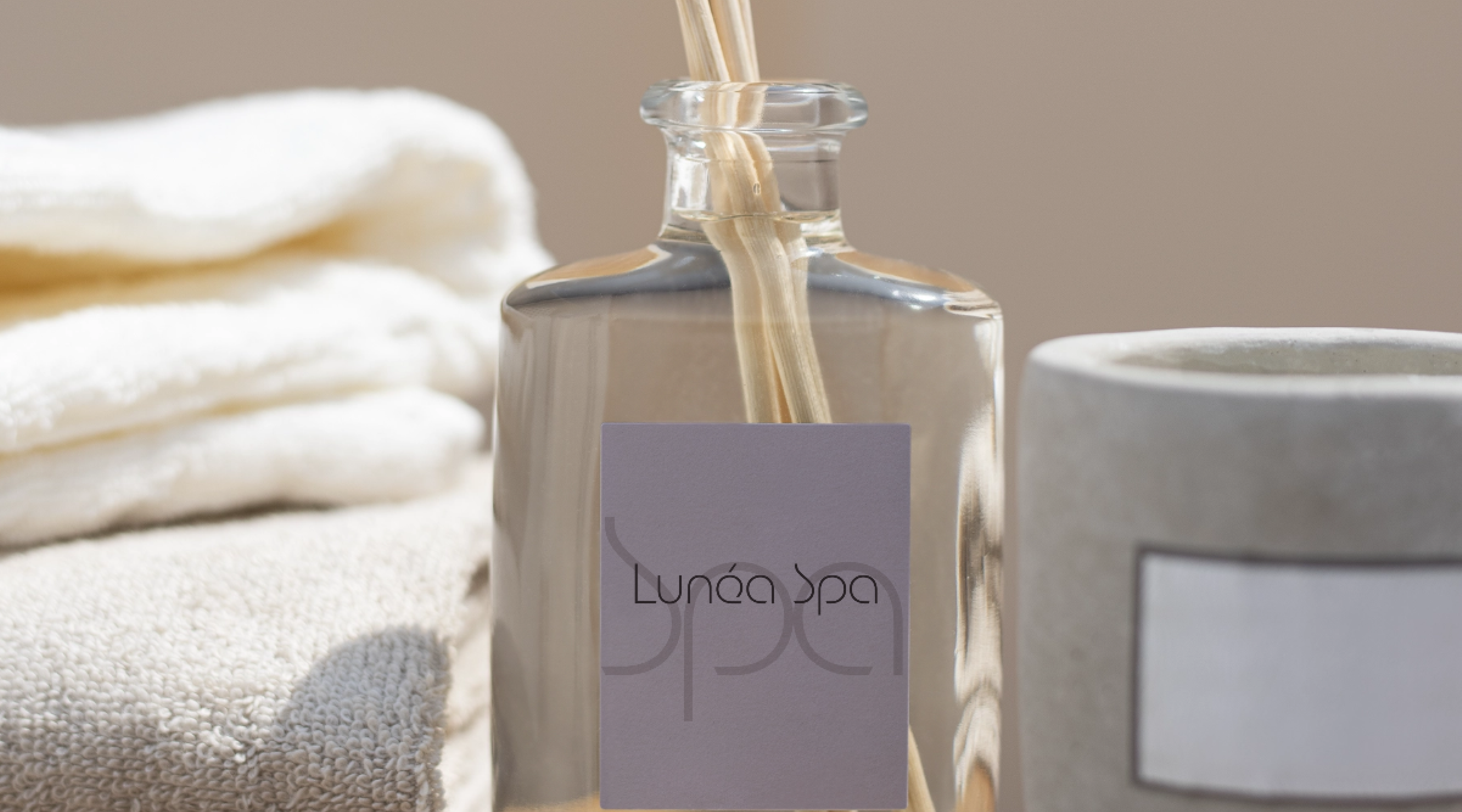 Флакон с логотипом Lunéa Spa на фоне мягких полотенец, минималистичный брендинг для спа-салона.