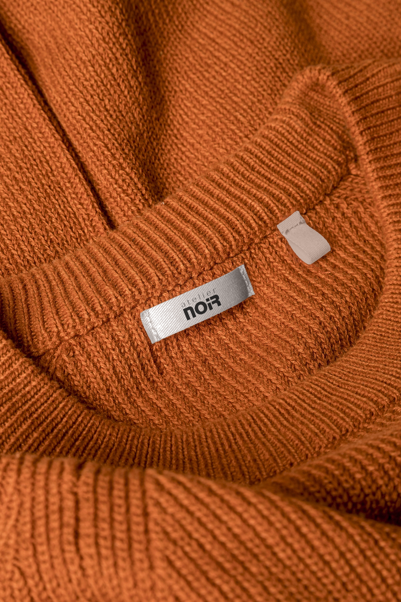 Лейбл Atelier NOIR на трикотажном джемпере теплого оттенка, брендирование одежды.